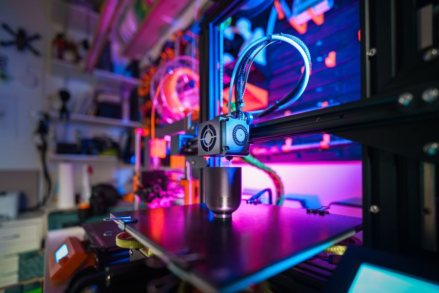 A desktop 3D printer printing a part under neon workshop lighting